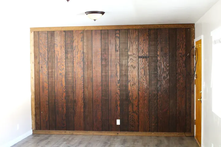 Feature wall with rich wood paneling, wood-finish flooring, white walls, and a semi-flush mount ceiling light