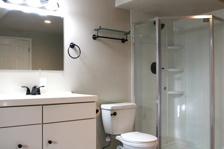 Bathroom featuring a corner shower enclosure, white vanity with black hardware, and an overhead vanity light fixture
