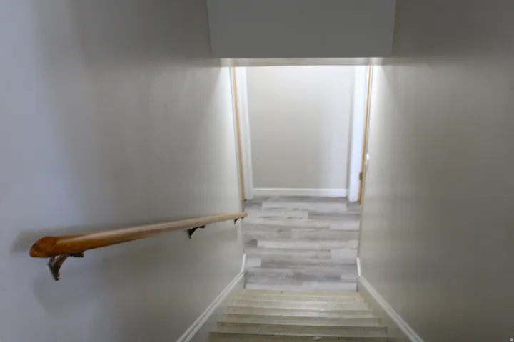 Stairwell to basement featuring a natural wood handrail, light gray wall paint, and white trim