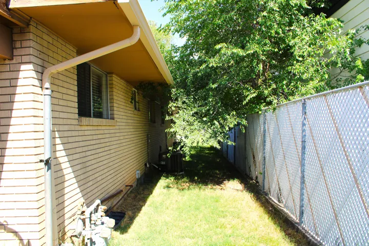 Side yard featuring a chain-link fence with privacy slats, mature trees, and a brick exterior
