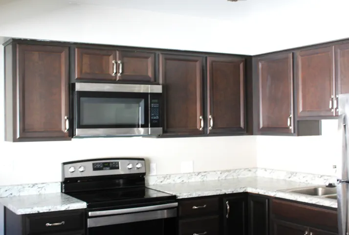Kitchen featuring dark wood-finish cabinetry, stainless steel microwave, stainless steel range, and light-toned countertops