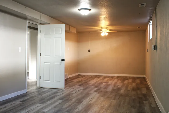 Spacious room featuring wood-finish flooring, light-toned walls, and a ceiling fan with integrated lighting