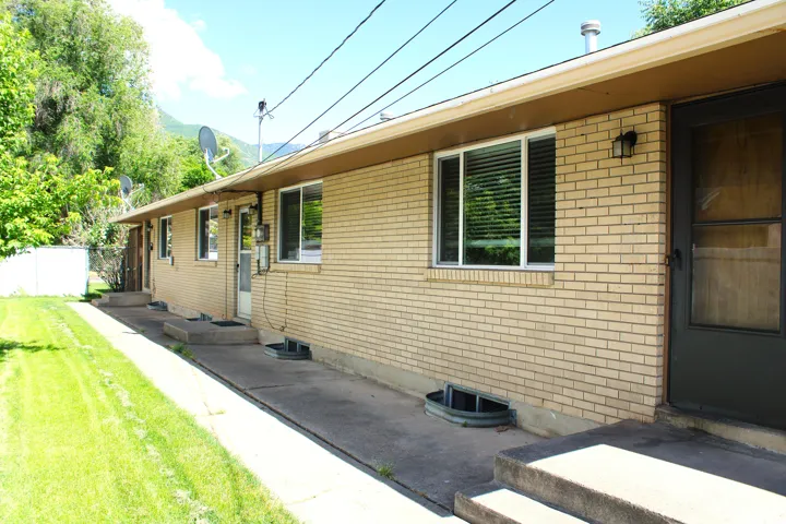 Light-colored brick exterior featuring multiple windows and entry doors, a flat roofline, and a concrete pathway