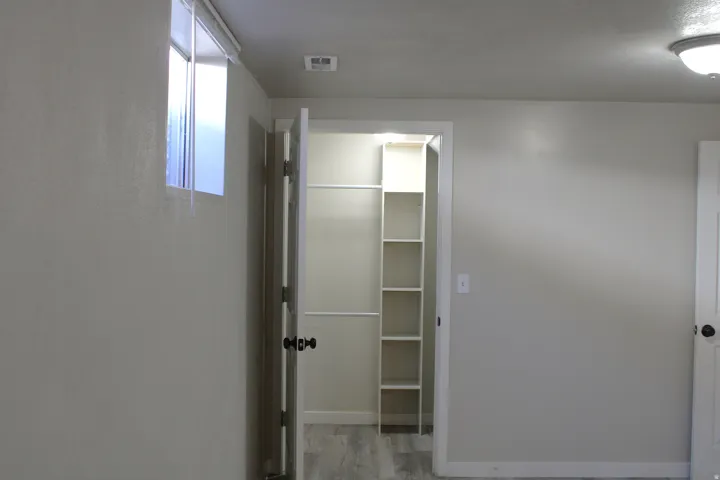 Interior room featuring a built-in closet with shelving, wood-finish flooring, a wall-mounted window, a flush mount ceiling light, and a white interior door with dark hardware