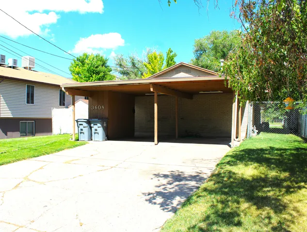 West side carport structure with a pitched shingle roof covering a concrete driveway