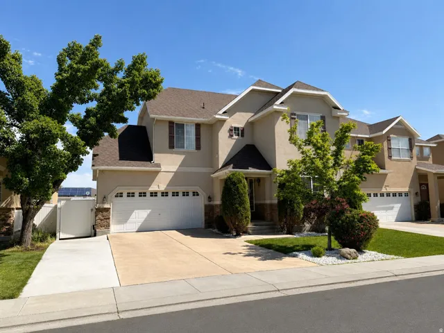 Stucco exterior with stone accents, brown composite shingle roof, white garage doors, and decorative window shutters