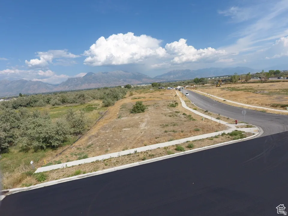 Paved streets and sidewalks bordering undeveloped land, with a backdrop of distant mountains
