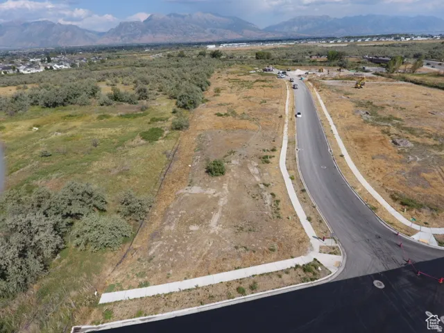 Expansive undeveloped land parcel featuring a paved road, established sidewalks, and distant mountain backdrops