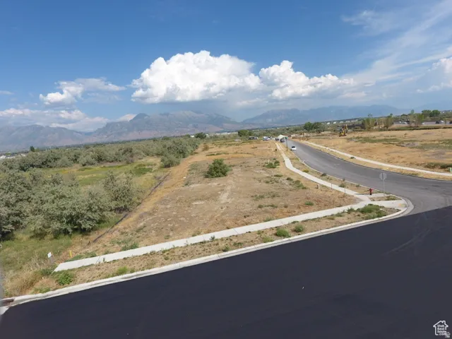 Paved streets and sidewalks bordering undeveloped land, with a backdrop of distant mountains