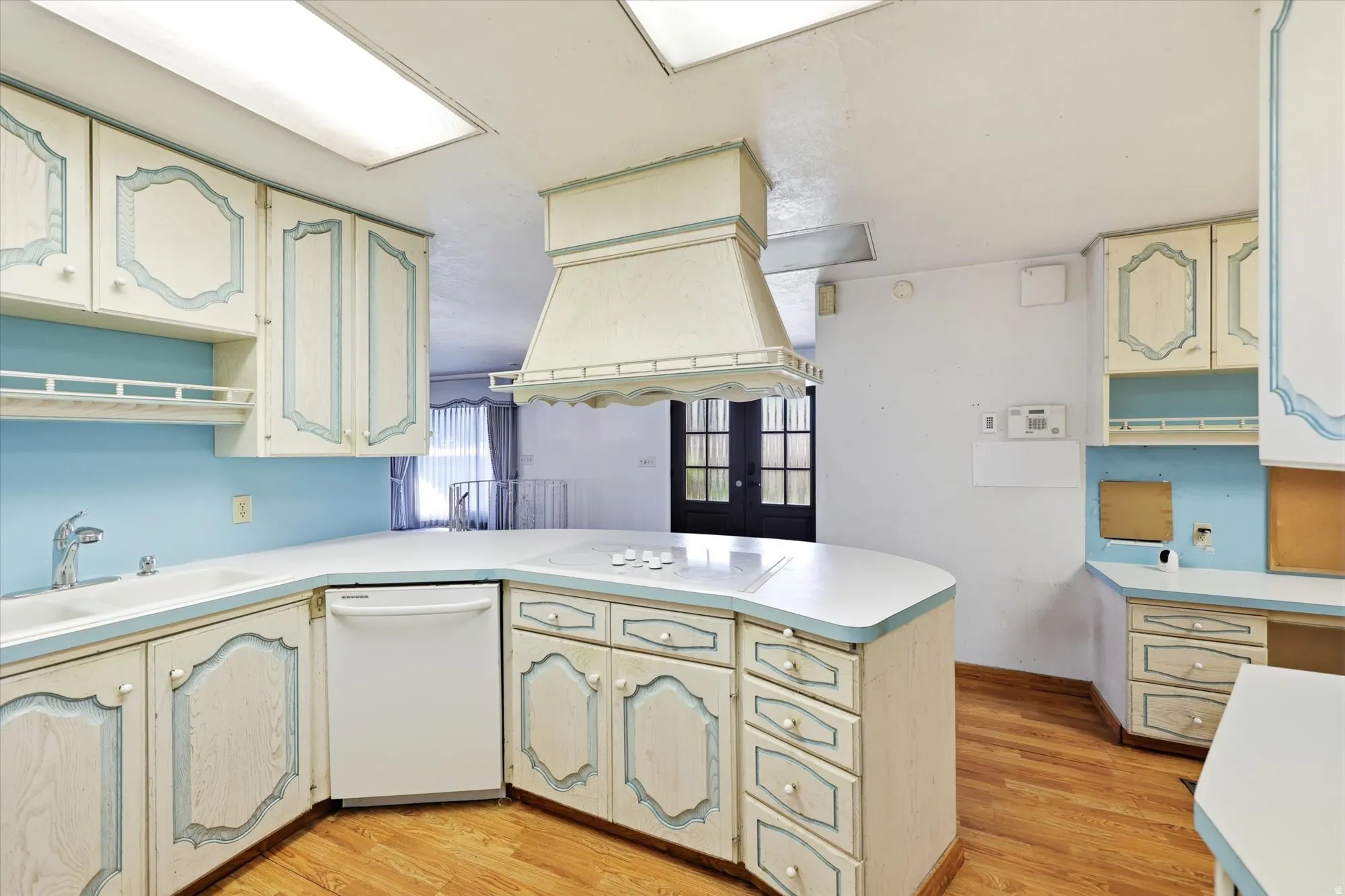 Kitchen featuring a built-in cooktop on a curved countertop, ample cabinetry with decorative detailing, a built-in dishwasher, and wood-finish flooring