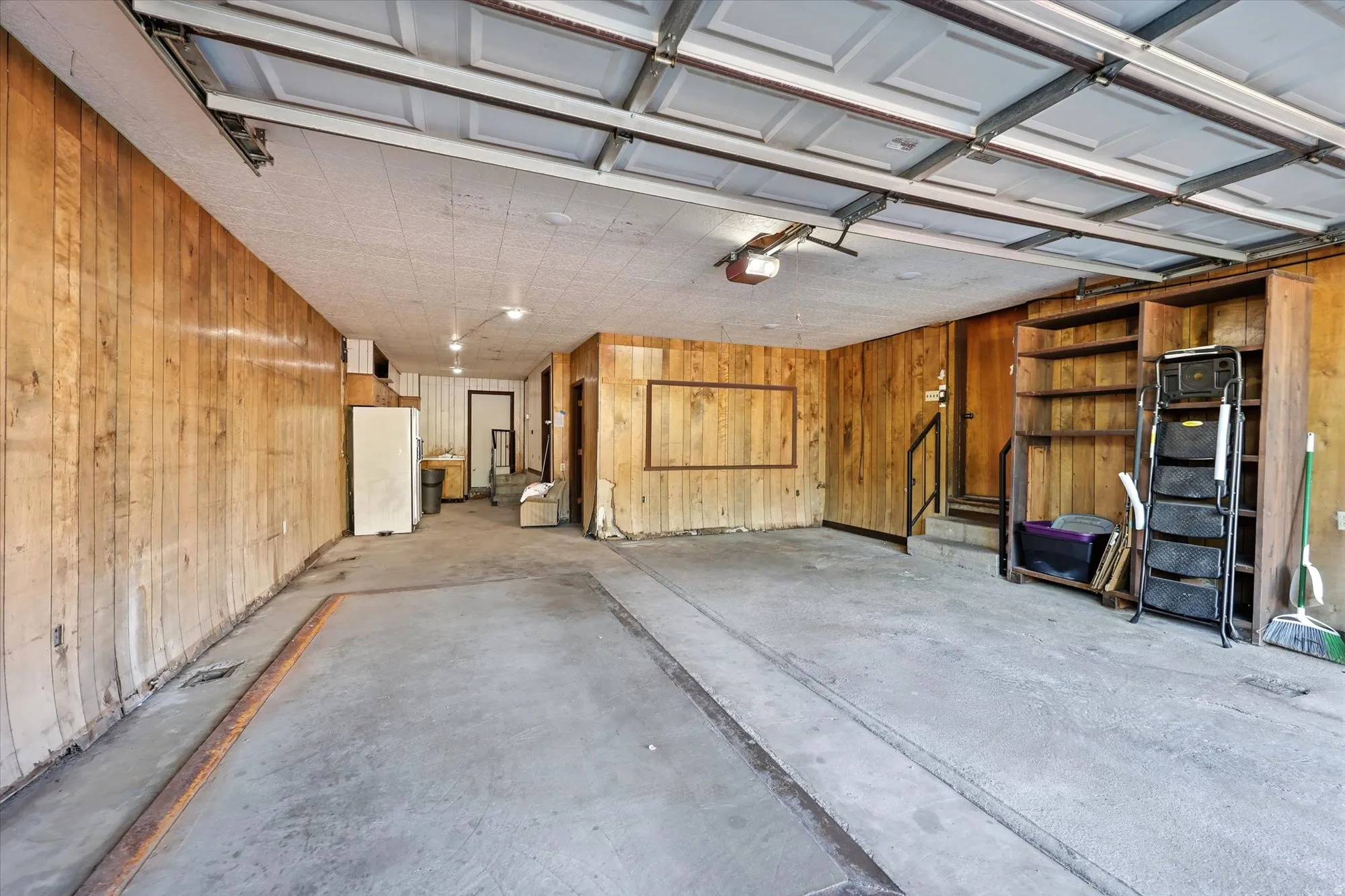 Spacious garage featuring concrete flooring, wood paneling, built-in shelving, and an overhead garage door