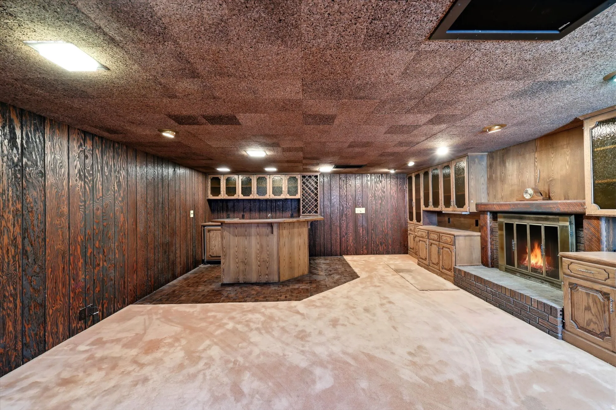 Spacious room featuring wood paneling, built-in wet bar with cabinetry and wine rack, brick-surround fireplace, and light-toned carpet flooring
