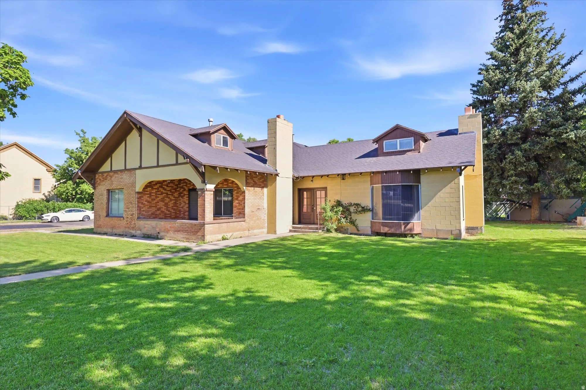 Craftsman-style exterior featuring a multi-gable roofline, brick and stucco siding, prominent front chimney, and a bay window