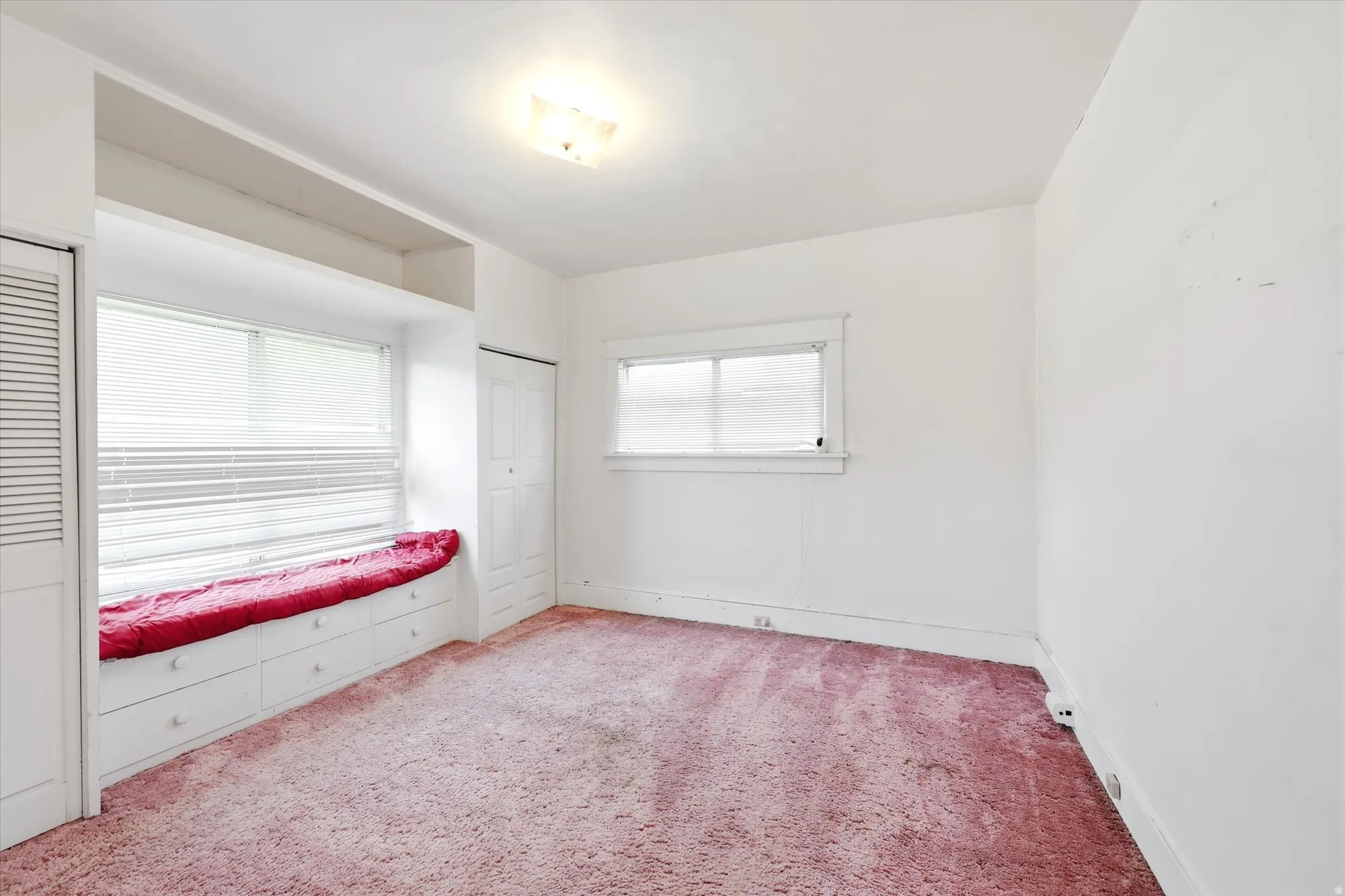 Room featuring a built-in window bench with integrated storage drawers, a broad window with horizontal blinds, and a flush-mount ceiling light fixture