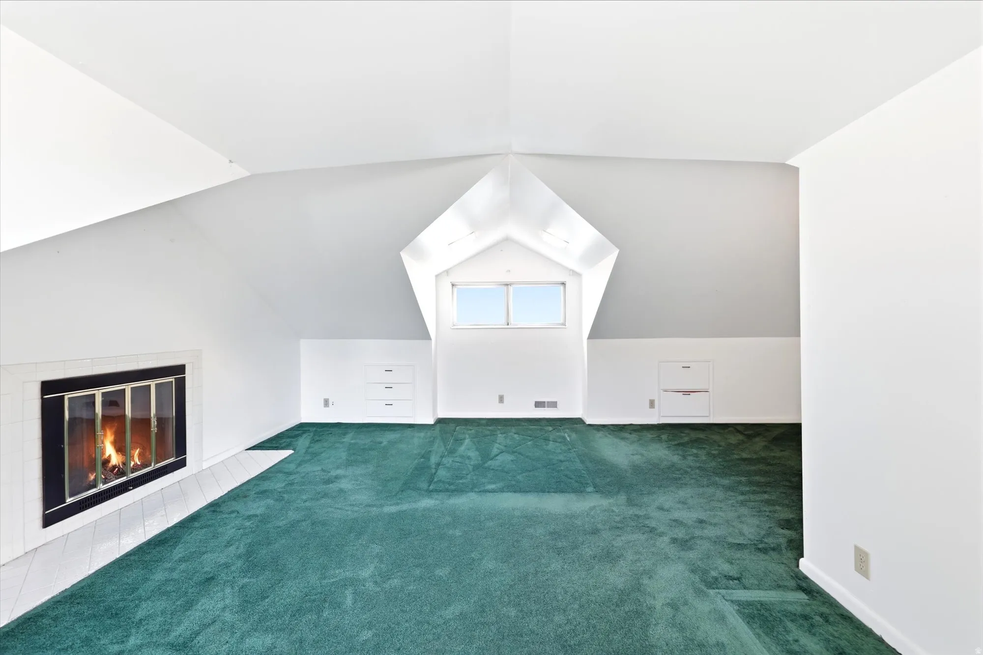 Spacious attic room featuring a fireplace with a white tile hearth, built-in storage drawers, and a window dormer