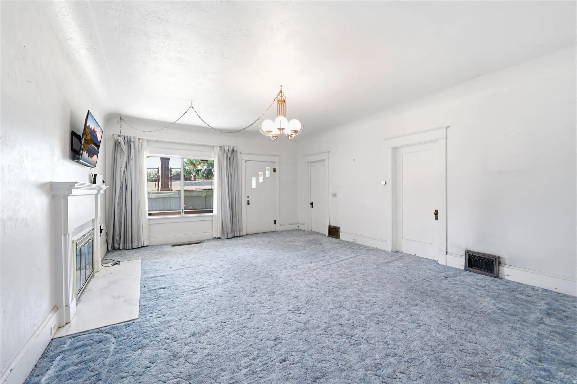 Spacious interior featuring a decorative fireplace with white surround, a large front window, and two paneled doors with black hardware