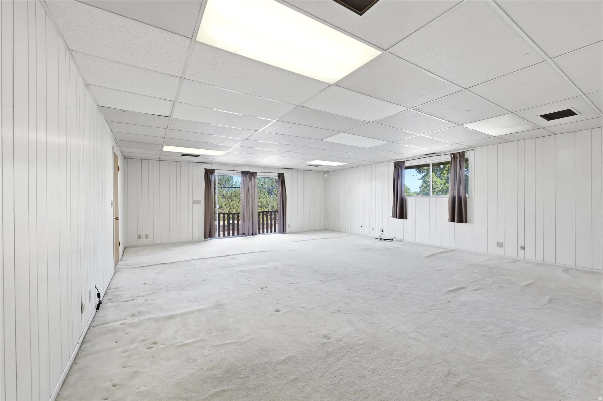Spacious room with white vertical paneling and light-colored carpet flooring