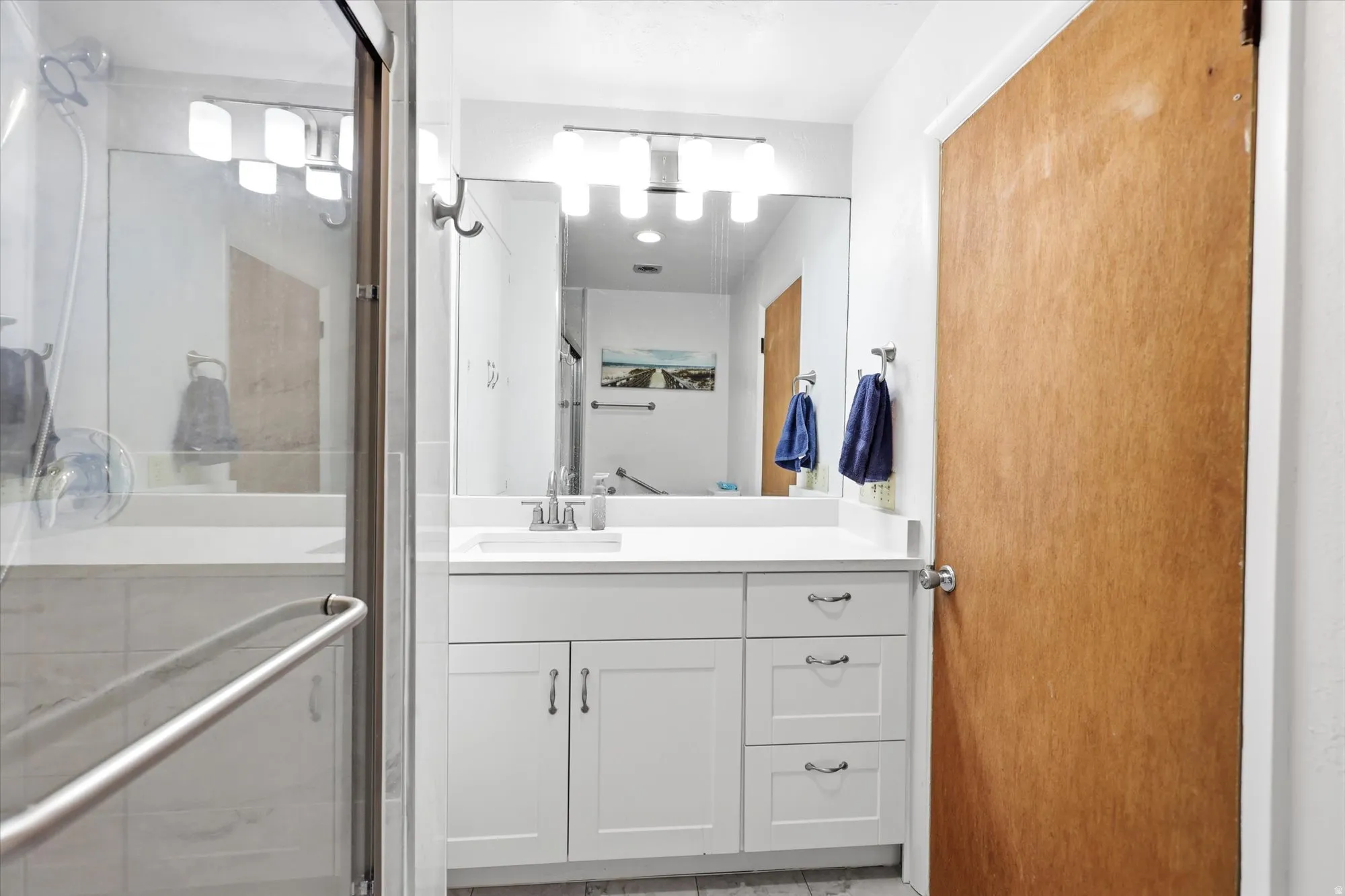 Modern bathroom featuring a single vanity with white cabinetry, a large mirror, and a glass-enclosed shower with tile surround