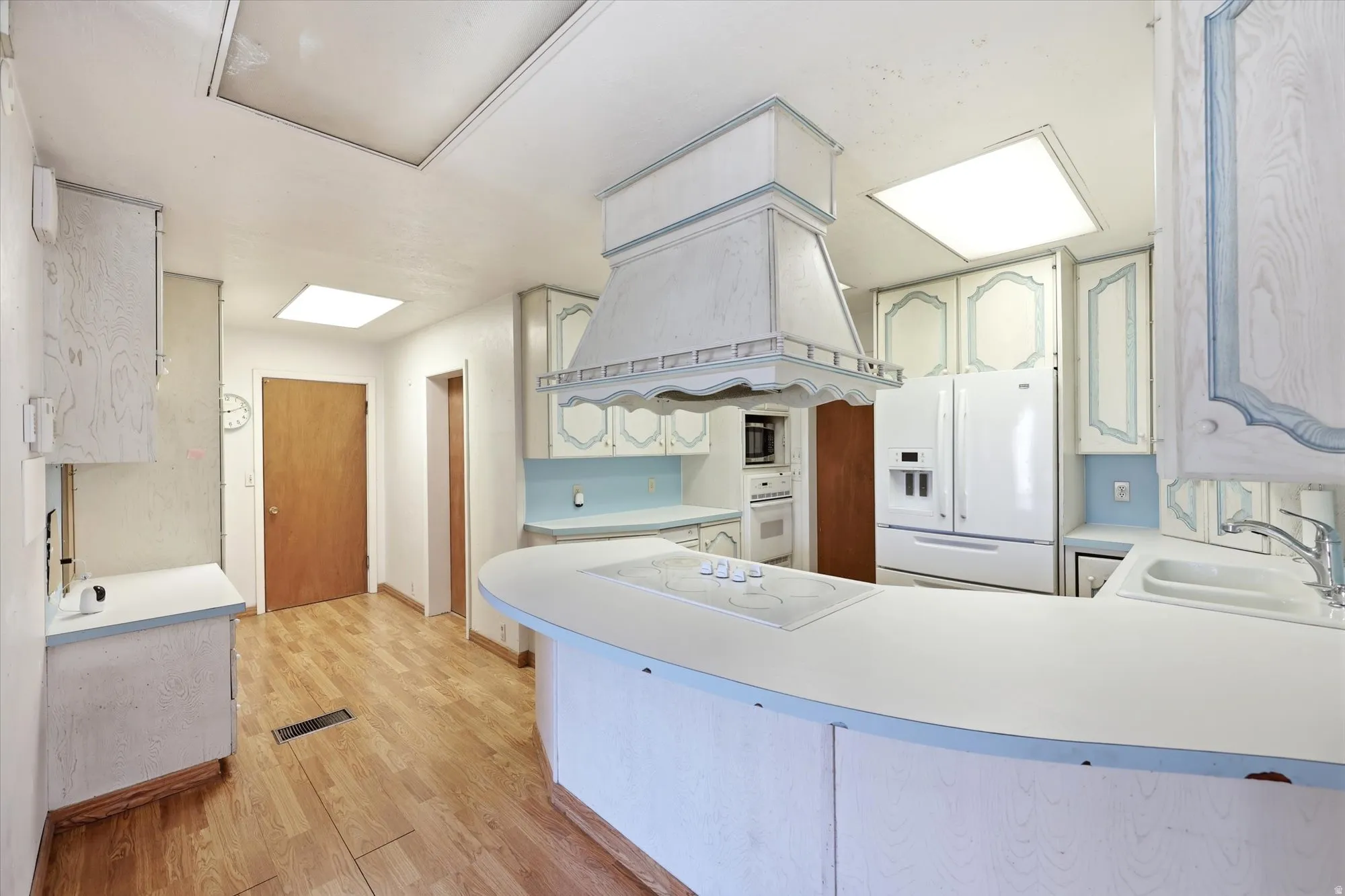 Kitchen featuring wood-finish flooring, recessed lighting, white cabinetry with blue accents, and a white refrigerator