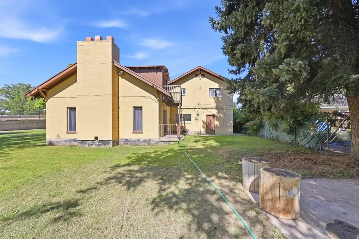 Expansive rear exterior featuring a two-story residence with a prominent chimney, a spacious lawn area, and mature trees providing shade
