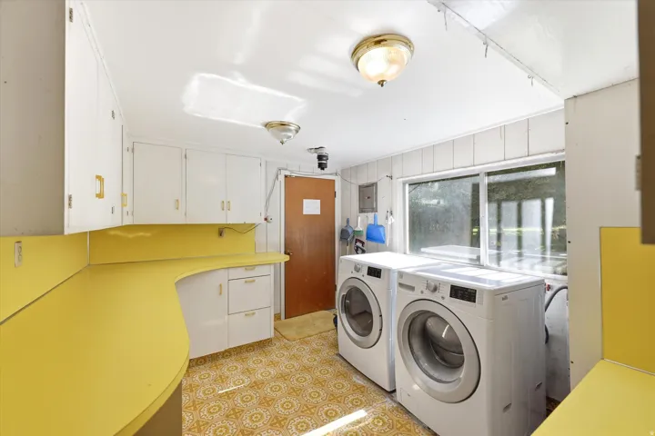 Utility room featuring wrap-around yellow countertops, ample white cabinetry, a large window, and patterned flooring