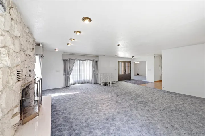 Spacious room featuring a prominent stone fireplace, recessed ceiling lighting, and a large window with sheer and opaque drapery