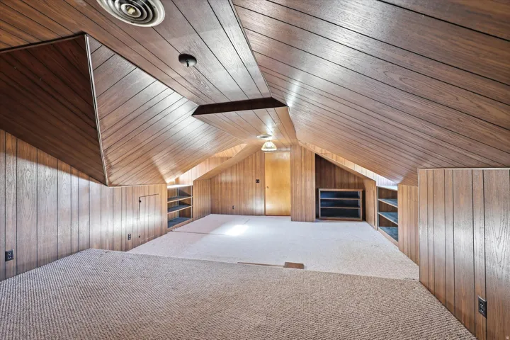 Carpeted attic space featuring wood-finish wall and ceiling paneling
