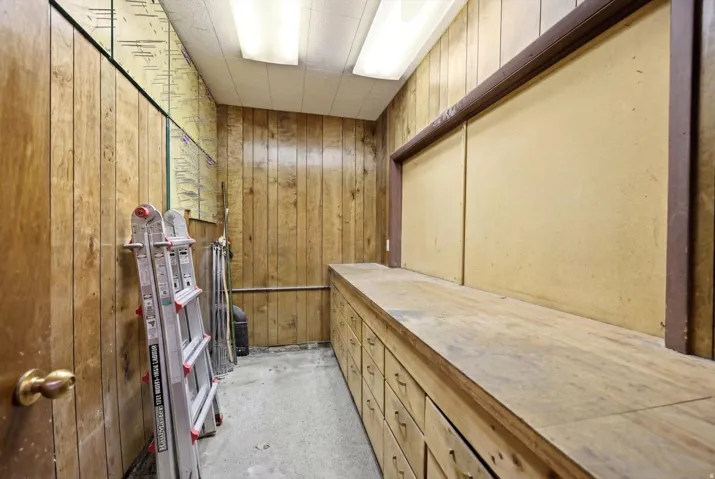 Utility room featuring wood paneling, extensive built-in cabinetry, a large workbench surface, and overhead fluorescent lighting