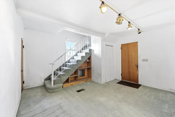 Carpeted living area featuring a wooden entry door, track lighting, and a staircase with built-in shelving