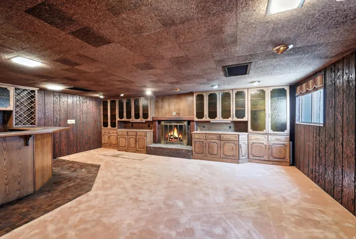 Spacious recreational area featuring a brick fireplace, built-in cabinetry with glass display fronts, wood paneling, a wet bar with a wine rack, and plush carpeting
