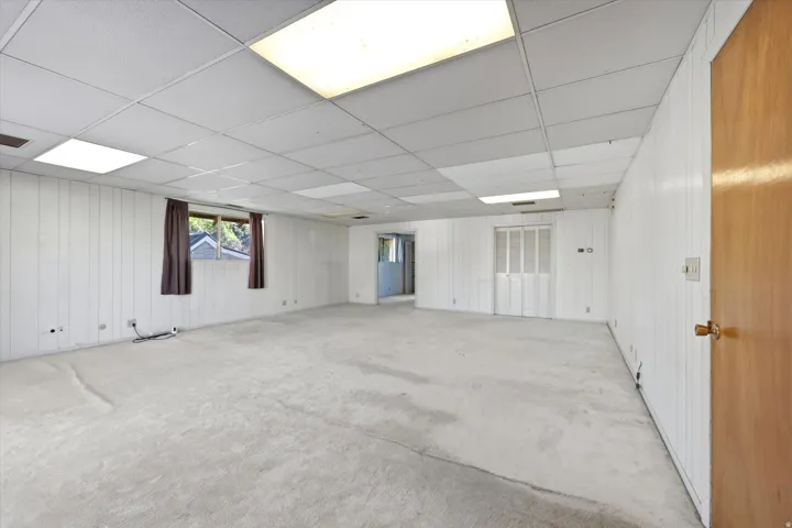 Spacious room featuring light-colored carpet, white vertical paneling, and a drop ceiling with integrated lighting