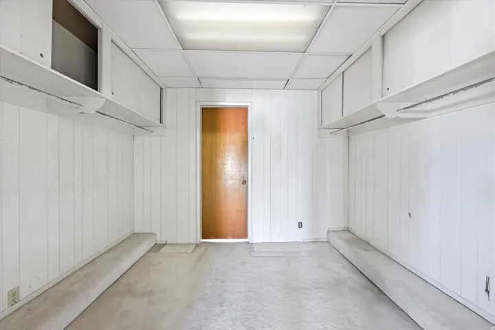 Room featuring white vertical paneling, a drop ceiling with fluorescent lighting, and a wood-finish door