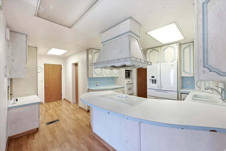 Kitchen featuring wood-finish flooring, recessed lighting, white cabinetry with blue accents, and a white refrigerator