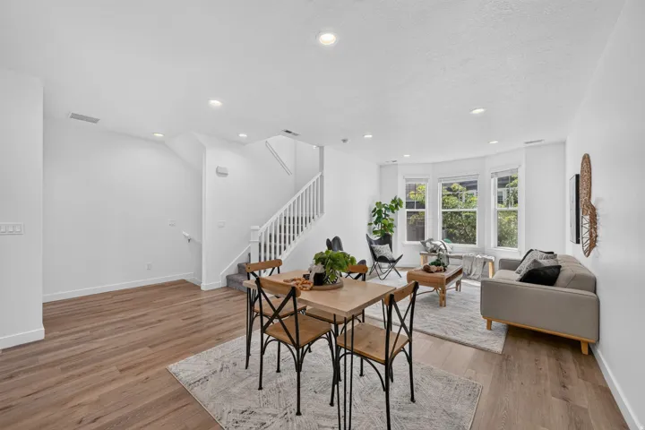 Open-concept living space featuring wood-finish flooring, recessed lighting, and a prominent staircase with white balusters