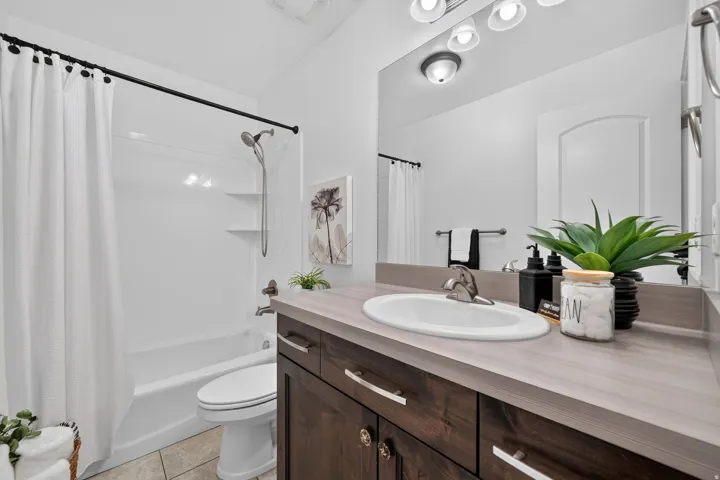 Bathroom featuring a white bathtub and shower combination with a curved shower curtain rod, a dark wood-finish vanity with a light countertop, an integrated sink, and a large mirror with overhead lighting