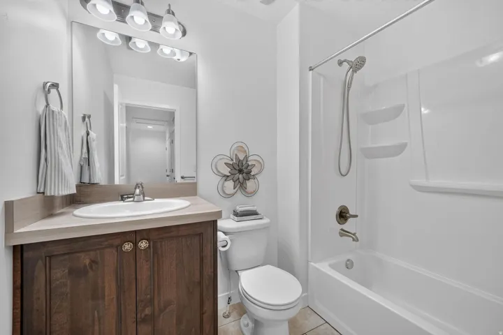 Full bathroom featuring a white tub and shower combination with bronze-finish fixtures, a single vanity with wood-finish cabinetry, a white oval sink, and a large mirror with overhead lighting