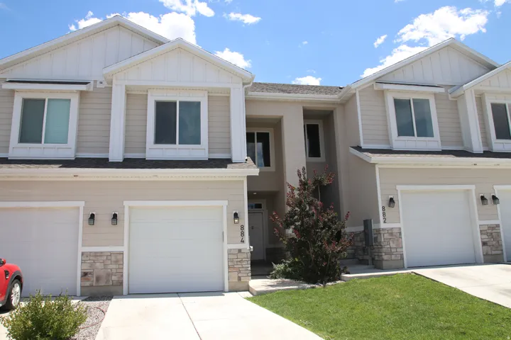 Neutral-toned townhouse exterior featuring an attached garage, stone accents, and light-colored siding