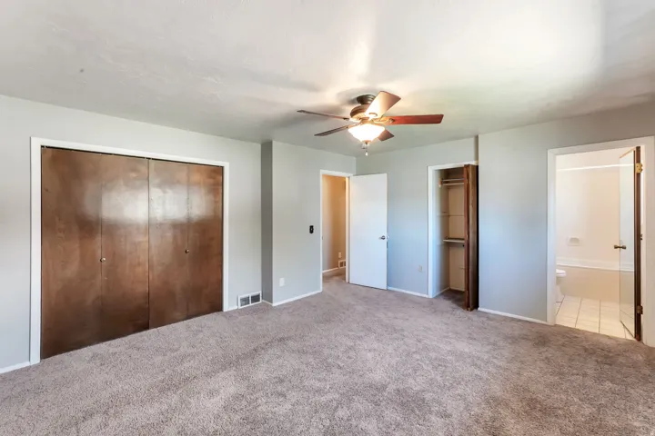Carpeted room featuring a ceiling fan, two closet spaces, and entryways to additional rooms
