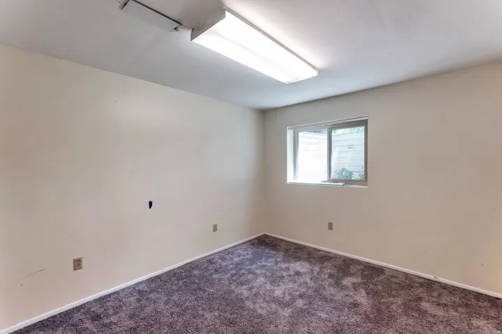 Carpeted room with a single window and overhead fluorescent lighting
