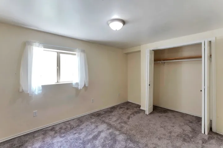 Bedroom featuring neutral wall paint, gray textured carpeting, a double-pane window, and a bi-fold door closet with an interior hanging rod