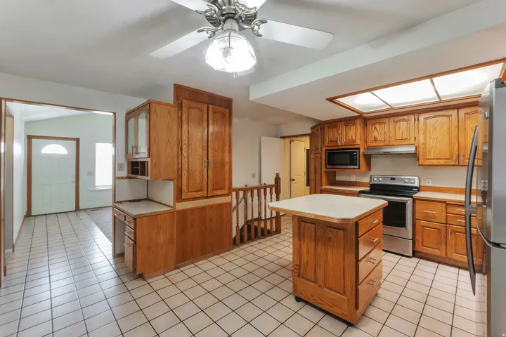 Kitchen featuring warm wood cabinetry, stainless steel appliances, a mobile island, and tile flooring