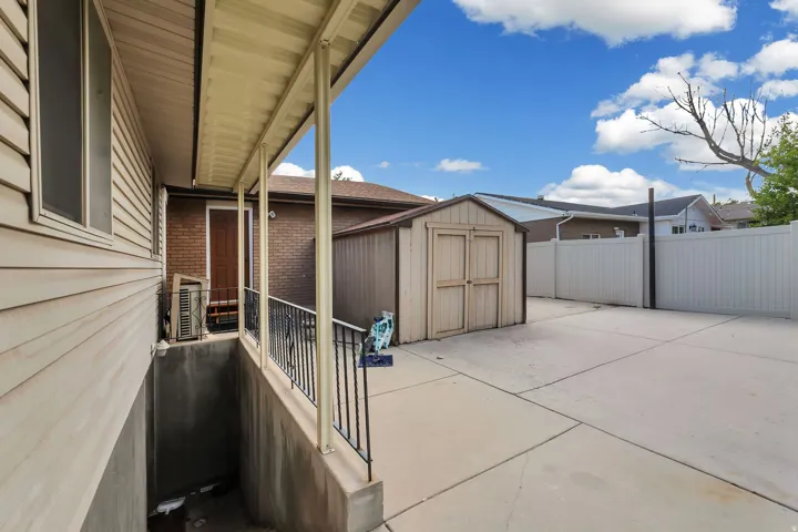 Expansive concrete patio area featuring a detached storage shed, a vinyl privacy fence, and a covered patio with metal railings
