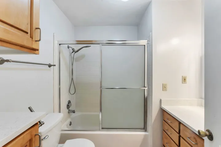 Full bathroom featuring a tub-shower combination with sliding frosted glass doors, white subway tile surround, and a chrome shower head
