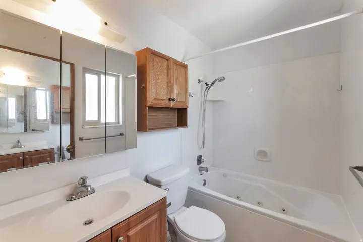 Bathroom featuring a single vanity with wood-finish cabinetry and integrated sink, a mirrored medicine cabinet, a toilet, a jetted bathtub, and overhead lighting