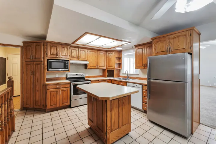 Kitchen featuring wood cabinetry, stainless steel appliances, a center island with countertop, and tile flooring