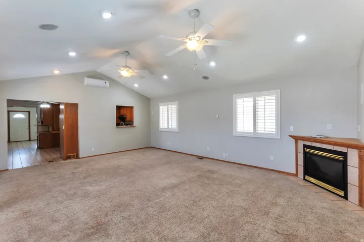 Spacious living area featuring vaulted ceilings with recessed lighting, two ceiling fans, and an integrated corner fireplace with a tiled surround