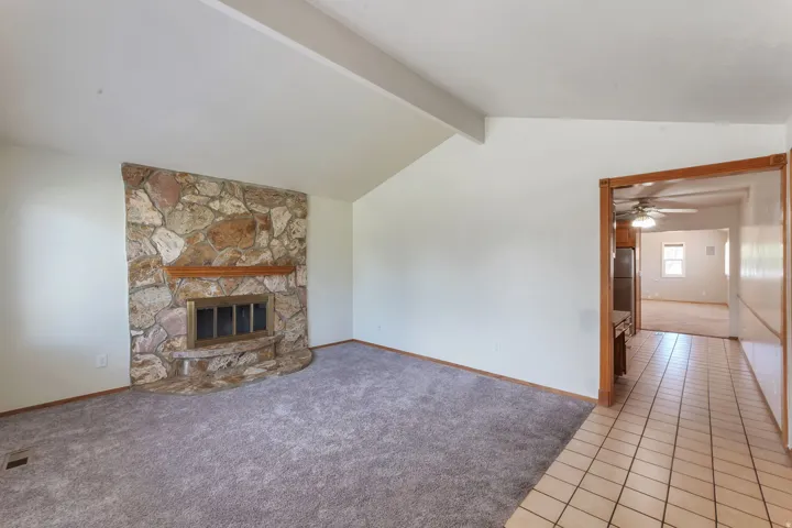 Stone-clad fireplace with wood mantle and hearth, vaulted ceilings, and gray carpet flooring