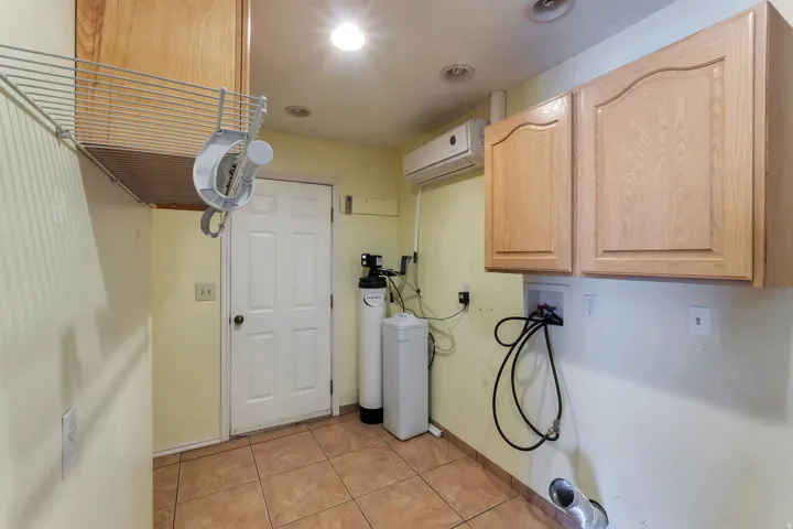 Utility room featuring durable tile flooring, wood-finish cabinetry, wire shelving, a white paneled door, and a wall-mounted air conditioning unit