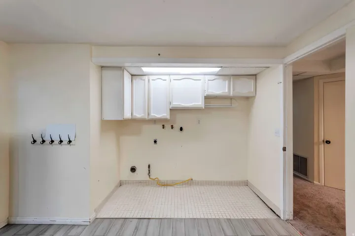 Utility area featuring white upper cabinetry, square tile flooring, wood-finish flooring, and a wall-mounted coat rack
