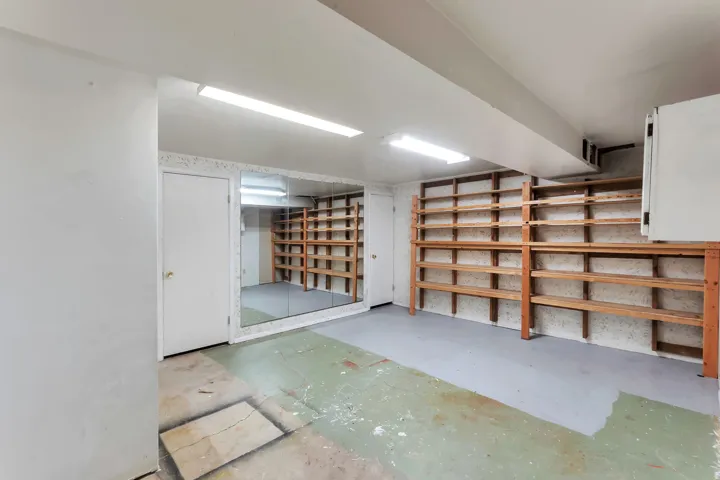 Spacious room featuring extensive built-in shelving, full-wall mirror, two doors, and fluorescent lighting